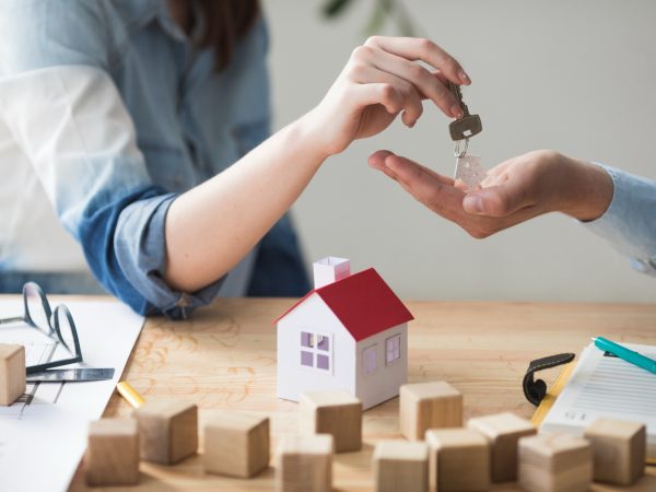 close-up-woman-s-hand-giving-house-key-man-wooden-table